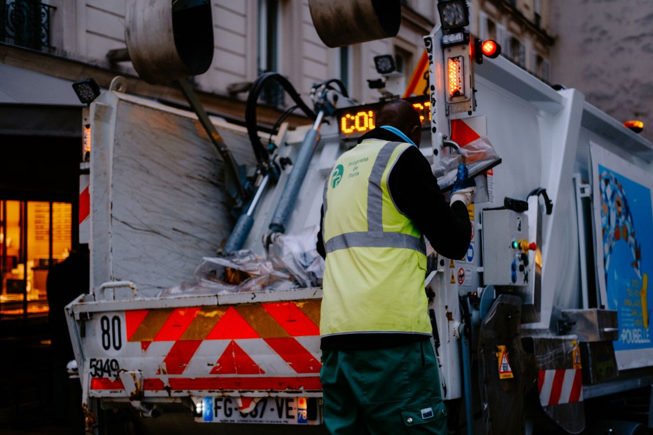 Services A garbage collector works on a city street, managing waste collection at dusk.