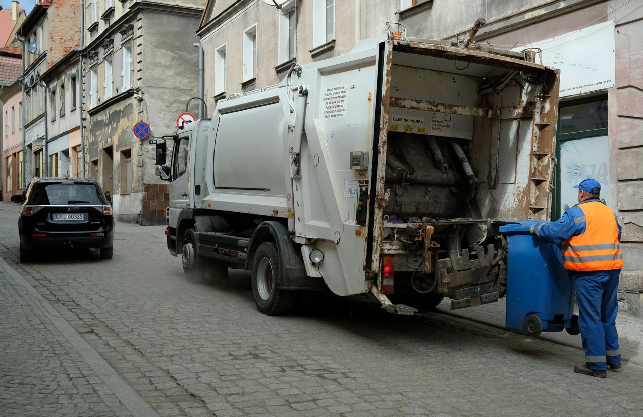 Services City street scene with garbage truck and worker handling waste bin.