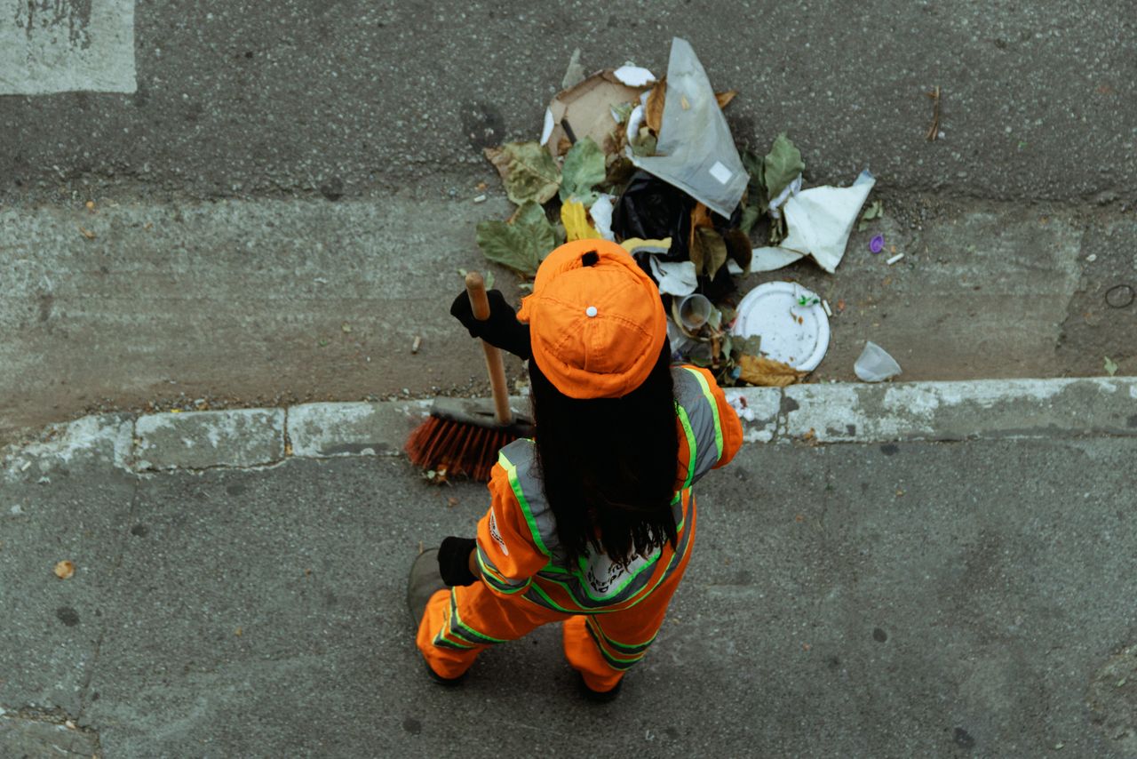 A street cleaner in an orange uniform sweeps debris from the roadside, ensuring cleanliness.