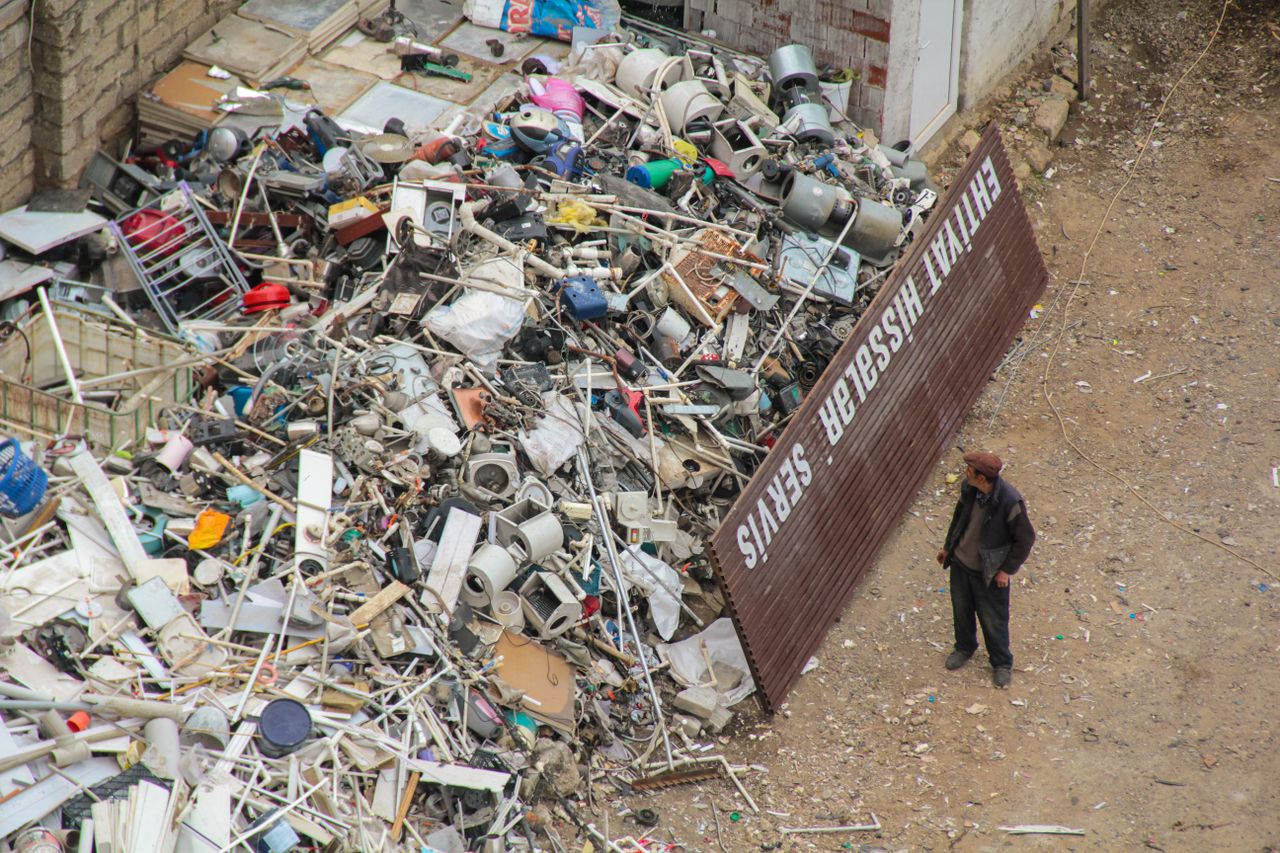 About A person inspecting a large pile of scrap metal and electronic waste in an outdoor junkyard.